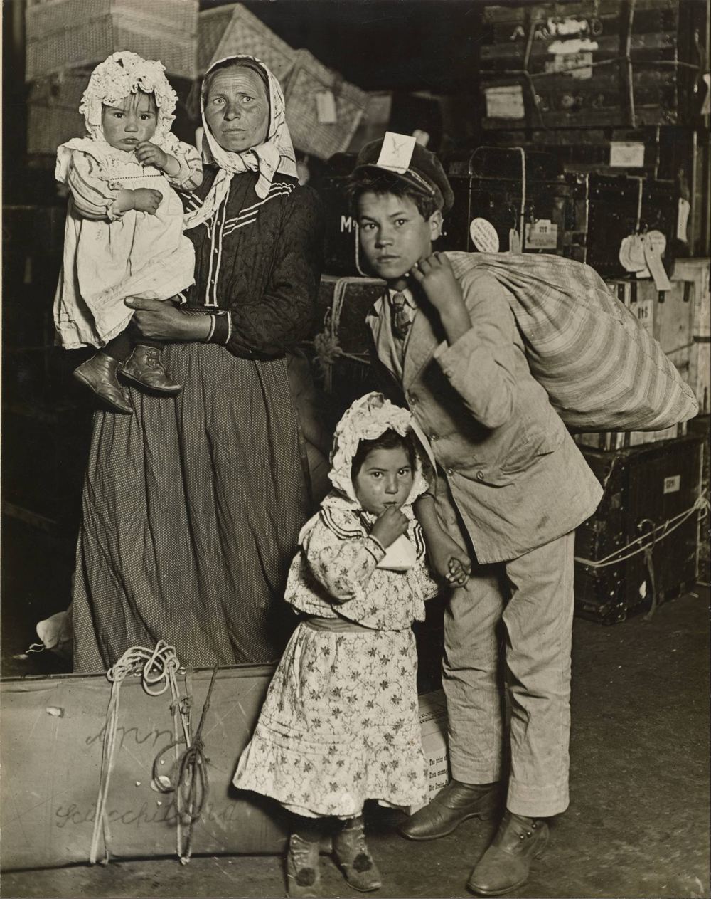 An immigrant family with children stands among trunks and bundles in the baggage room at Ellis Island in 1905