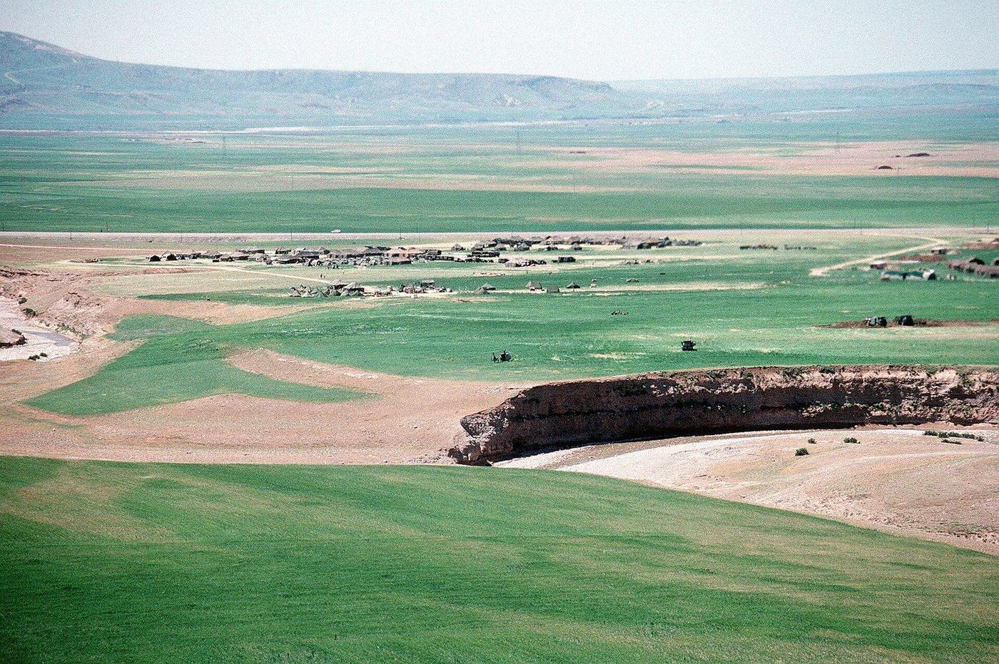 Rows of tents spread across green fields below a ridge in northern Iraq